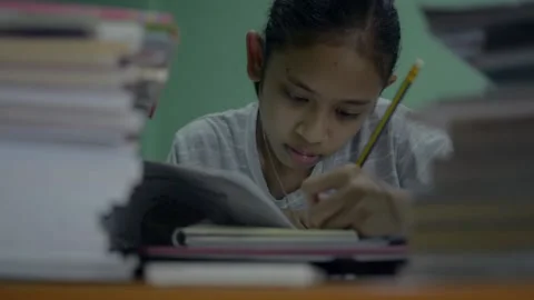 High schoolgirl doing homework with stack of textbook on the desk at night. Stock Footage 150533541