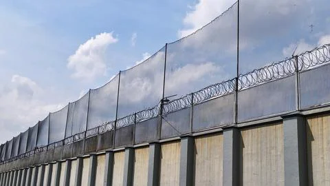 High-security prison concrete wall fence with netting and barbed wire Stock Photos