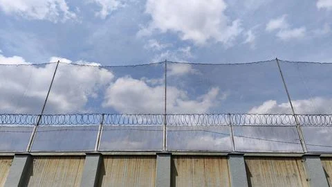 High-security prison concrete wall fence with netting and barbed wire Stockfoto's
