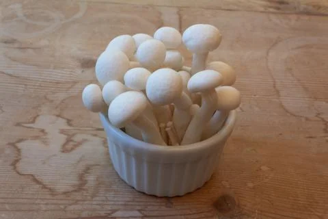 High side view of a small dish of white mushrooms, centered on old wood Stock Photos