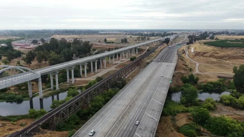 High-speed rail viaduct with arched river bridge runs parallel to a freeway Stock Footage 337670448