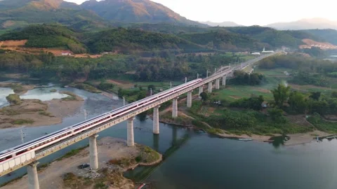High-speed train crossing a railway bridge over a river amid mountains Stock Footage 343919267