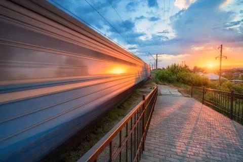 High speed train in motion on the railway station at sunset in summer. Movi.. Stock Photos