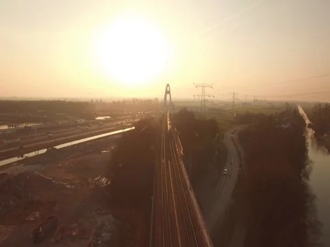 High speed train passing by on a bridge at a highway with traffic, sunset. Stock Footage 75406267