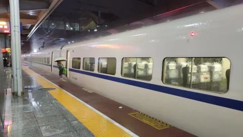 High speed train standing at the plaform while a Man comes out with umbrella Stock Photos