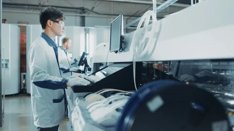 On High Tech Factory Asian Engineer Uses Computer for Programming Robotic Arm Stock Footage 98191284