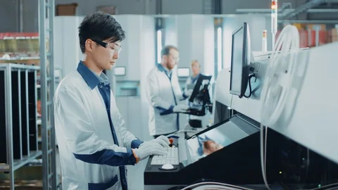 On High Tech Factory Asian Engineer Uses Computer for Programming Robotic Arm Stock Footage 98191822