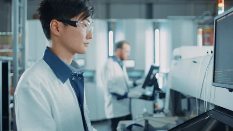 On High Tech Factory Asian Engineer Uses Computer for Programming Robotic Arm 動画素材 98192029