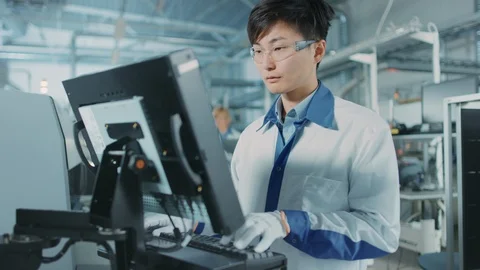 On High Tech Factory Asian Engineer Uses Computer for Programing Robot Video stock 98196192