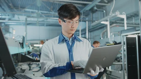 On High-Tech Factory Asian Engineer Uses Laptop Computer for Programming Machine Stock Footage 98197320