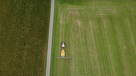 High top-down aerial of a red tractor spreading slurry beside a maize field Video stock 343416319