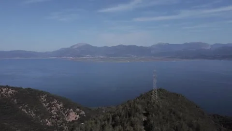 High view of blue coastal water beside rocky forested mountains and powerlines Stock Footage 344094757