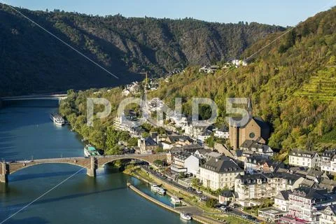 High view of riverside village with stone church and steep hillside slopes with Stock Photos