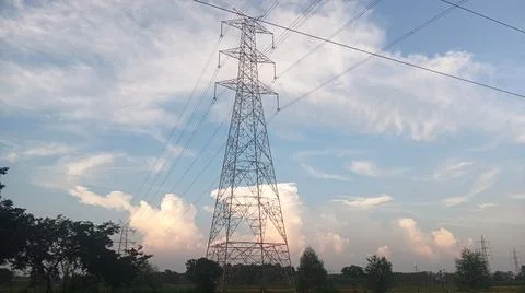 High-voltage electrical transmission tower against a blue sky with clouds Stock Photos
