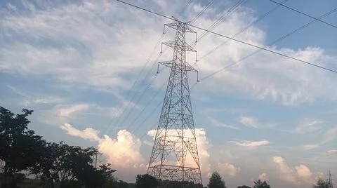 High-voltage electrical transmission tower against a blue sky with clouds Stock Photos