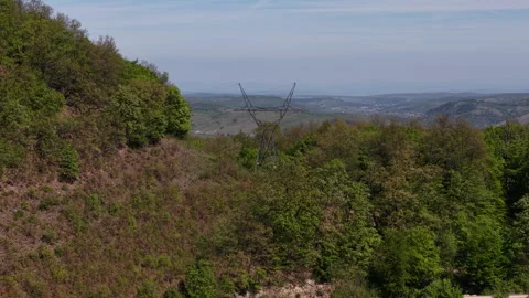 A high-voltage electricity pylon stands prominently on a lush green hillside 스톡 동영상 334139111