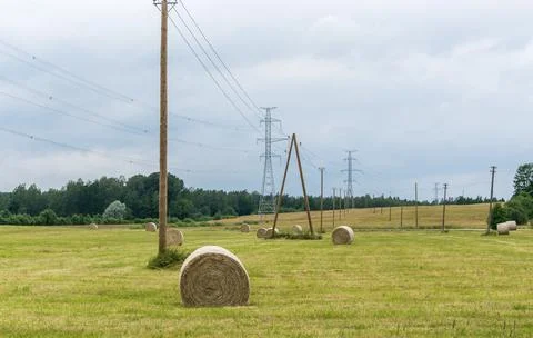 .High voltage line passes through a field with rolls of hay. Stock Photos