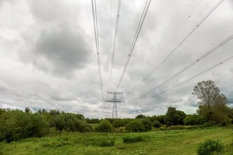 High voltage overhead power line. Green meadow with a cloudy sky Stock Photos