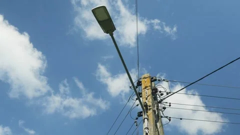 High voltage pole and street lamp against blue sky Stock Footage 343539679