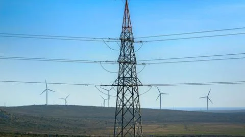 High voltage power line against rotating windmill wind turbines in valley. .. Stock Photos