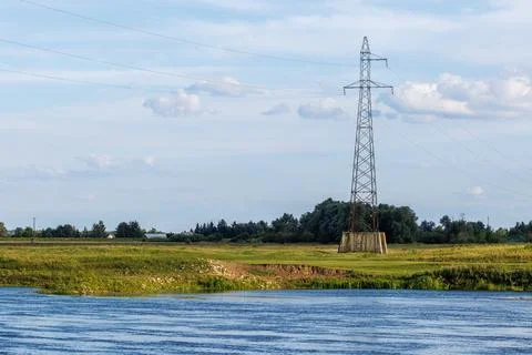A high voltage power line pylon standing in a green field next to a wide ri.. Stock Photos