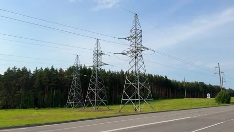 High voltage power line pylons along a road near a pine forest Vidéo 336796668