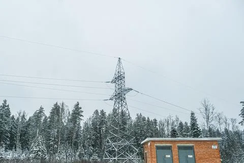 High voltage power line tower and brick building in a winter forest in overcast Stock Photos