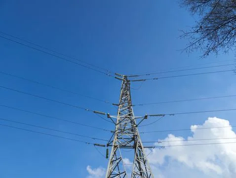 High voltage power line tower stands against bright blue sky with few clouds Stock Photos