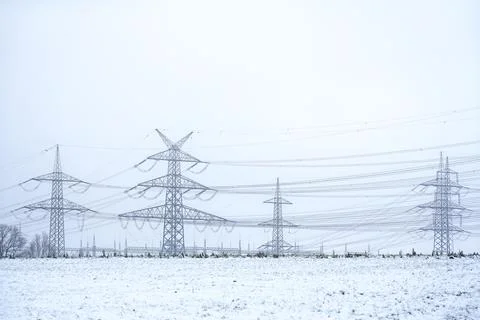 High voltage power lines and transmission towers in winter snow field Photos