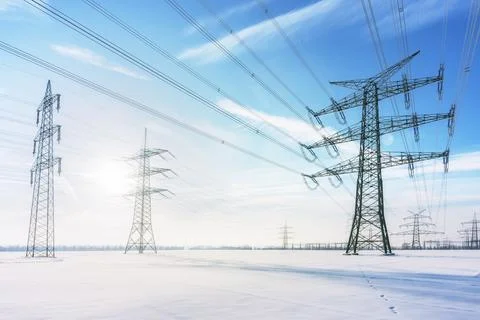 High voltage power lines and transmission towers in deep winter snow field Stock Photos