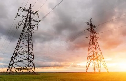 High-voltage power lines passing through a green field of wheat, on the backg Stock Photos