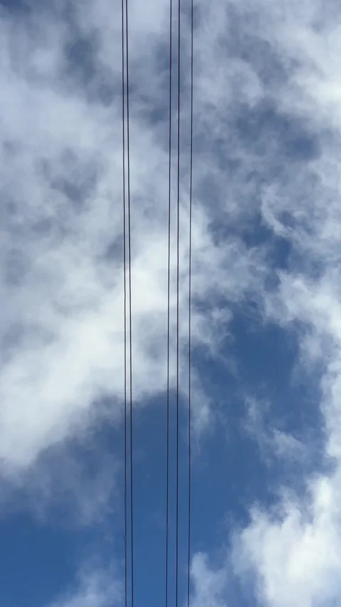High voltage power lines running vertically against a deep blue sky with wh.. Stock Footage 324842462
