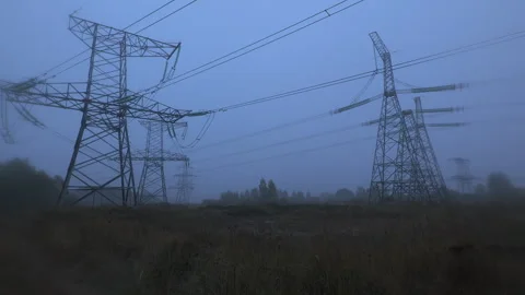 High voltage power lines stretch across a foggy landscape at dawn Stock Footage 291322429