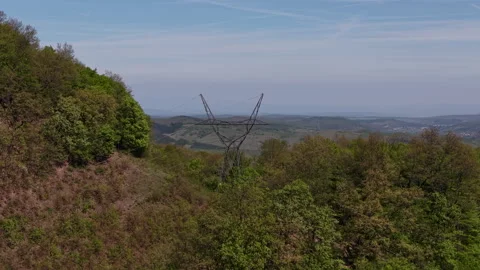 A high-voltage power pylon stands prominently on a forested hillside Stock Footage 334138837