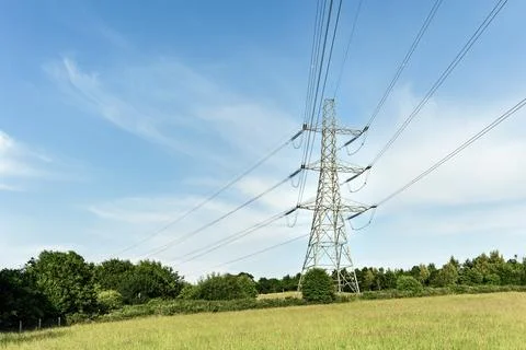 High Voltage Pylon and Power Lines in a Grassy Field Against a Blue Sky Stock Photos