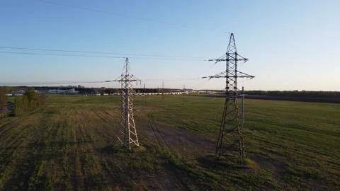 High-voltage towers stand in a field against the backdrop of a road filled with Stock Footage 319894833