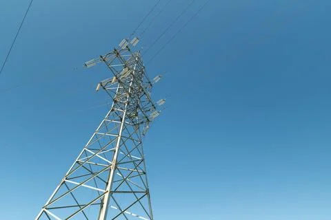 High voltage transmission tower from low angle against clear blue sky with .. Stock Photos