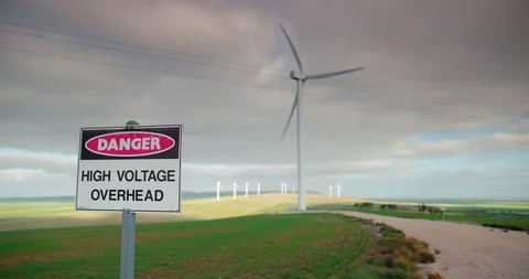 High voltage warning sign with blurred-out wind farm in background. Stock Footage 98843142