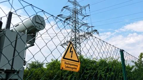 High Voltage Warning Sign with Electrical Pylon in Background Stock Photos
