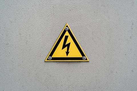 High voltage yellow triangle warning sign on gray metal wall Stock Photos
