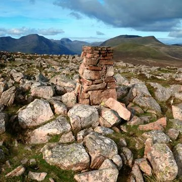 Highland mountain peak featuring a stacked stone pillar with distant mountain ra Stock Photos
