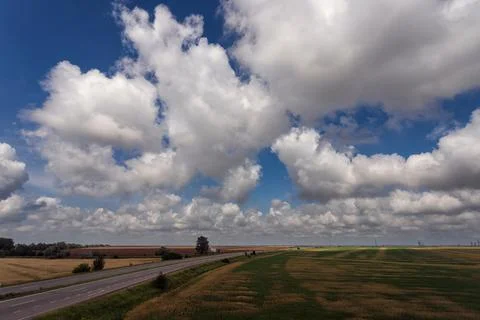 Highway among fields under a beautiful sky with white clouds Stock Photos