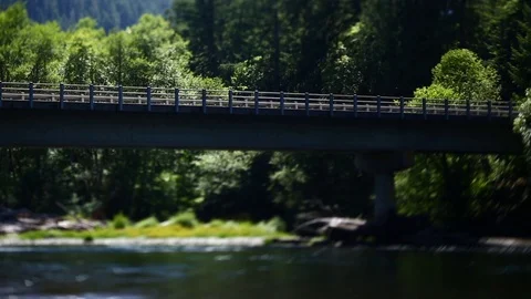HIGHWAY BRIDGE OVER RIVER WITH WATER FLOWING PAST AND TREES BLOWING IN THE WIND Stock Footage 80694363