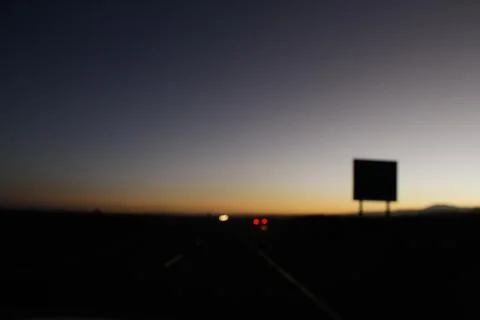 Highway in dusk with headlights and road sign silhouette Stock Photos