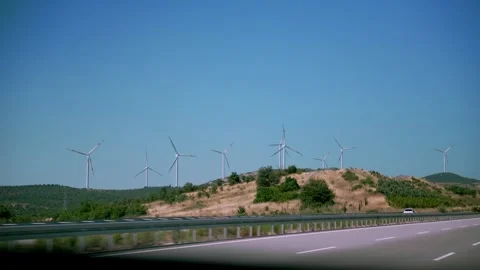 Highway passing by wind farm with multiple wind turbines on a grassy hillside Stock Footage 278731768