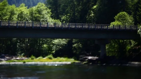 HIGHWAY ROAD BRIDGE OVER RIVER TRUCKS DRIVE WATER FLOWING TREES BLOWING IN WIND Stock Footage 80694978