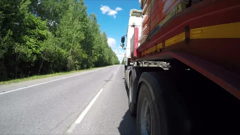 On the highway through the forest, a semi-truck is driving, carrying a cargo on  Stock Footage 162000731