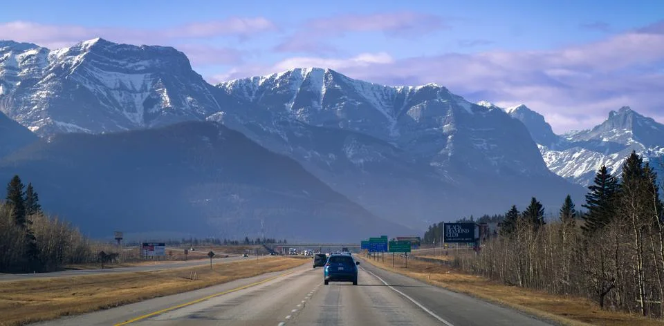 Highway traffic heading toward dramatic snow covered mountain peaks Stock Photos
