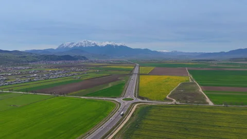 Highway traffic through green fields and snowy mountains, aerial pull back Stock Footage 337465377