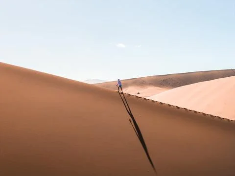 Hiker ascends rust red dune ridge at Sossusvlei near Deadvlei, Namibia Stock Photos